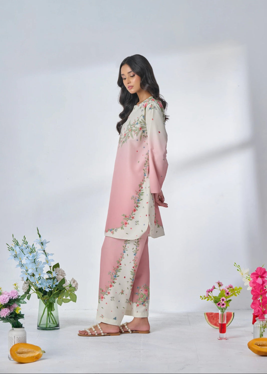 Woman wearing a pink floral outfit with decorative flowers and vases on a white background